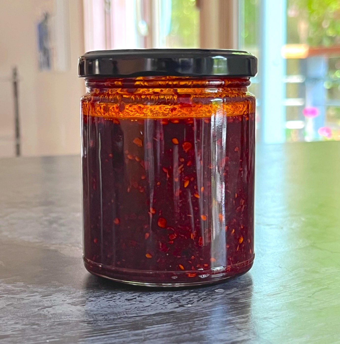 A jar of Saucy Girl chili crisp, deep red with a layer of bright orange chili oil on top and a black lid.